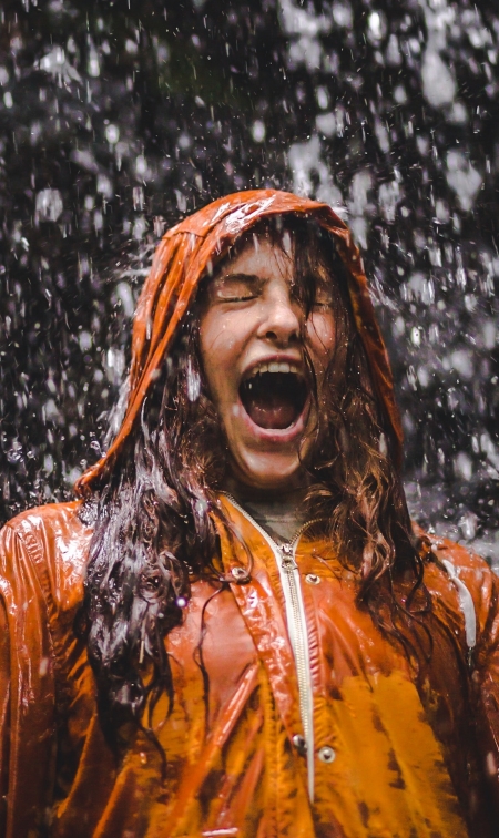 Woman wearing raincoat, surprised by rain