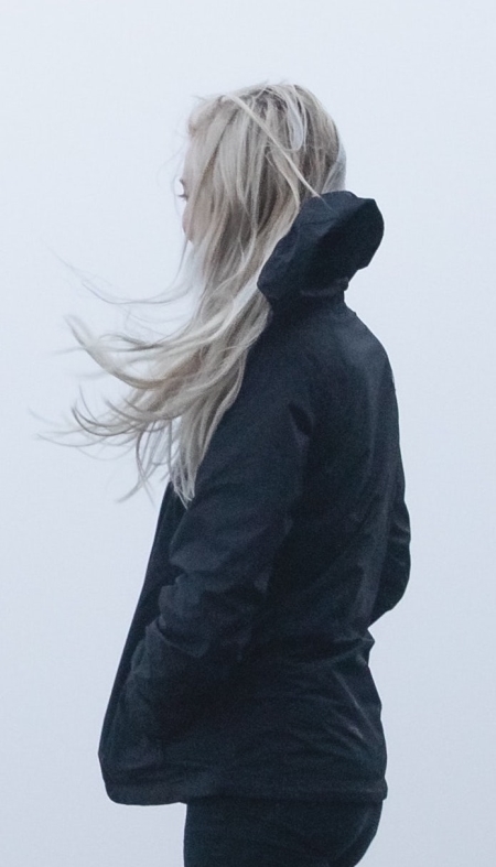 Blond woman wearing black rain jacket facing foggy weather