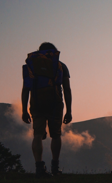 Man with backpack facing a pink sun rise
